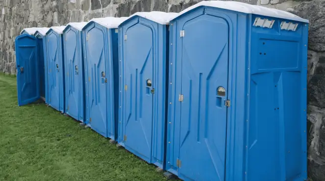 Row of blue portable toilets lined up on grass against a stone wall for event sanitation in Indianapolis, IN