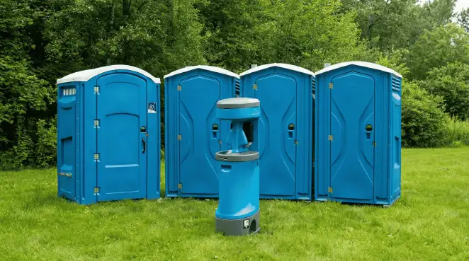 Four blue portable toilets and a matching hand washing station on grass near trees, a common sight at local outdoor events in Indianapolis, IN