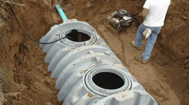 Septic tank installation showing a technician compacting soil around a new poly septic tank in an excavation pit in Indianapolis, IN
